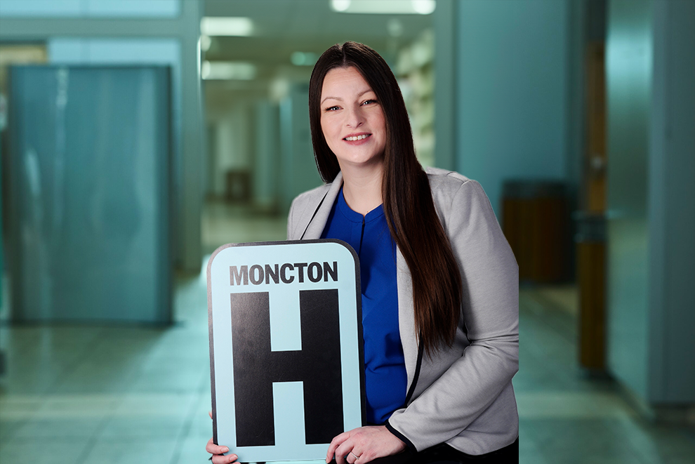 Angela Landry tient une pancarte H et sourit à la caméra