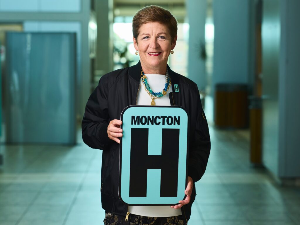Carol Chapman Holding H Sign and Smiling at camera