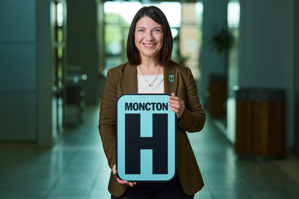 Ginette Goulet Holding H Sign and Smiling at camera