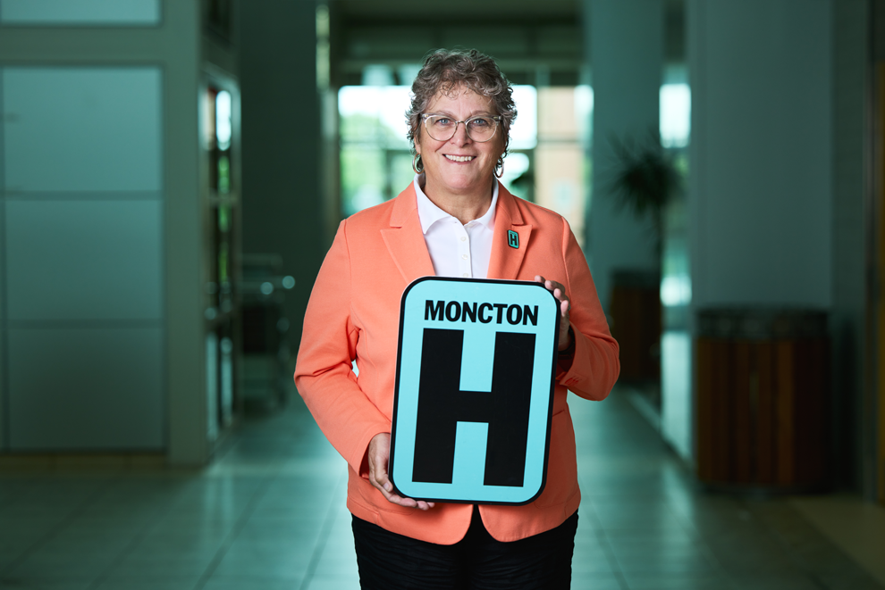 Jacqueline Bloom tient une pancarte H et sourit à la caméra