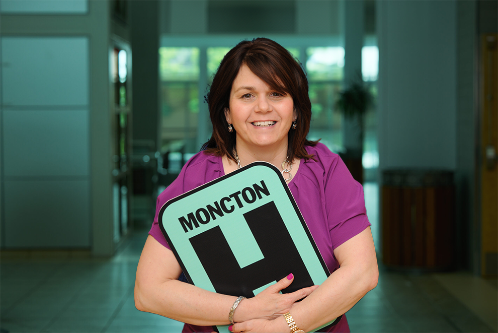 Janice Leger tient le panneau H et sourit à la caméra