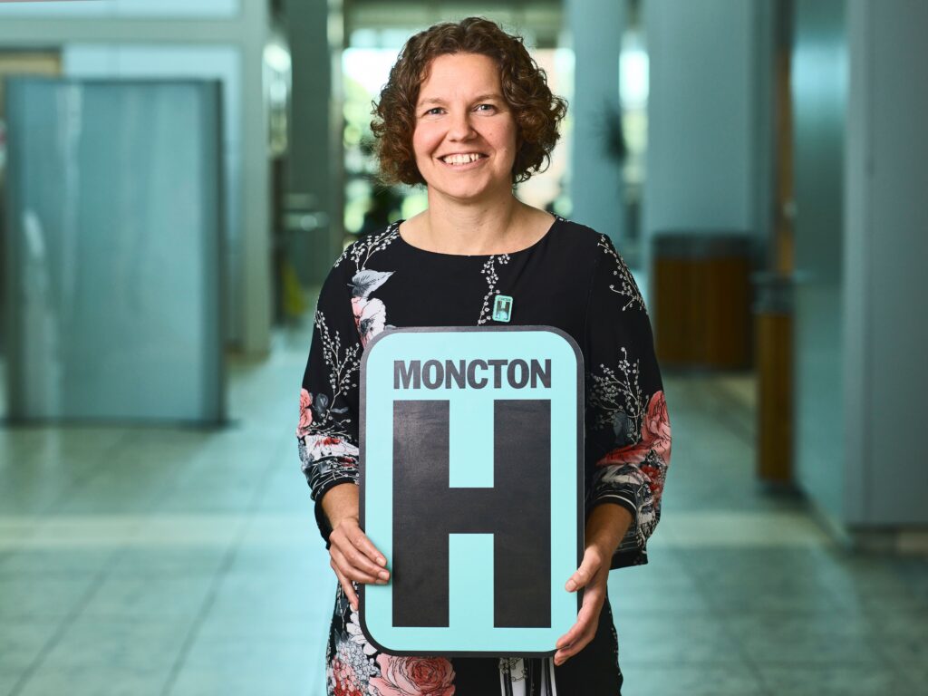 Josie Marks Holding H Sign and Smiling at camera