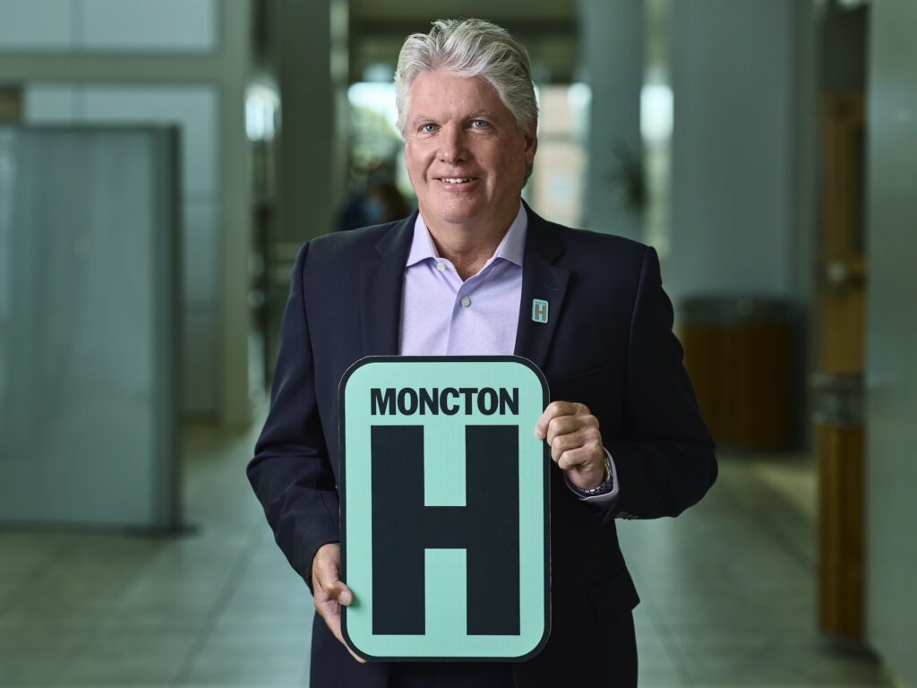 Shane Esson Holding H Sign and Smiling at camera