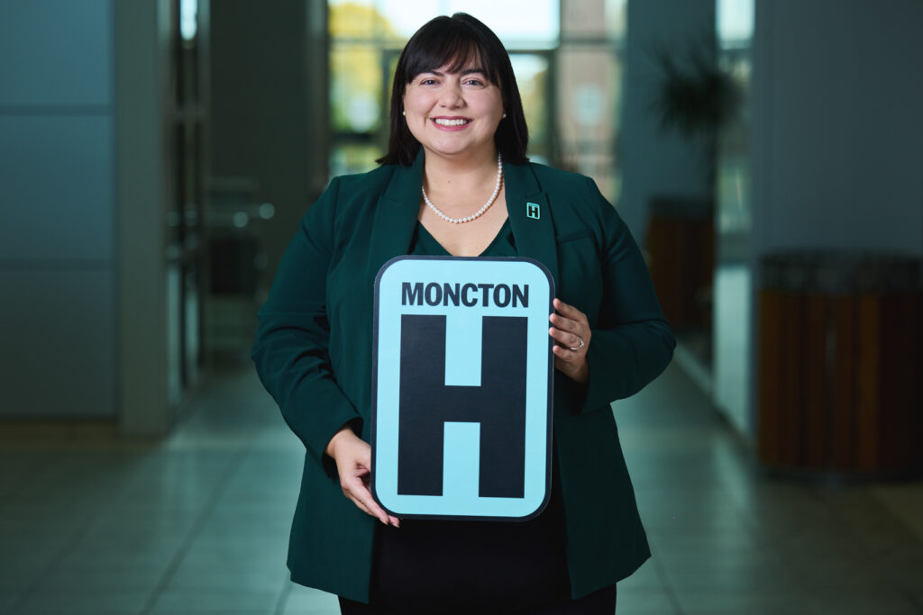 Frances LeBlanc Holding H Sign and Smiling at camera